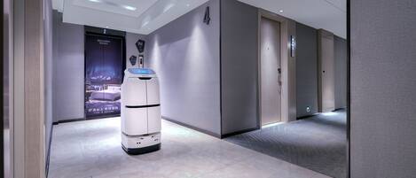 A modern hotel corridor with a self-service kiosk, a digital display, and a door with an emergency exit sign.