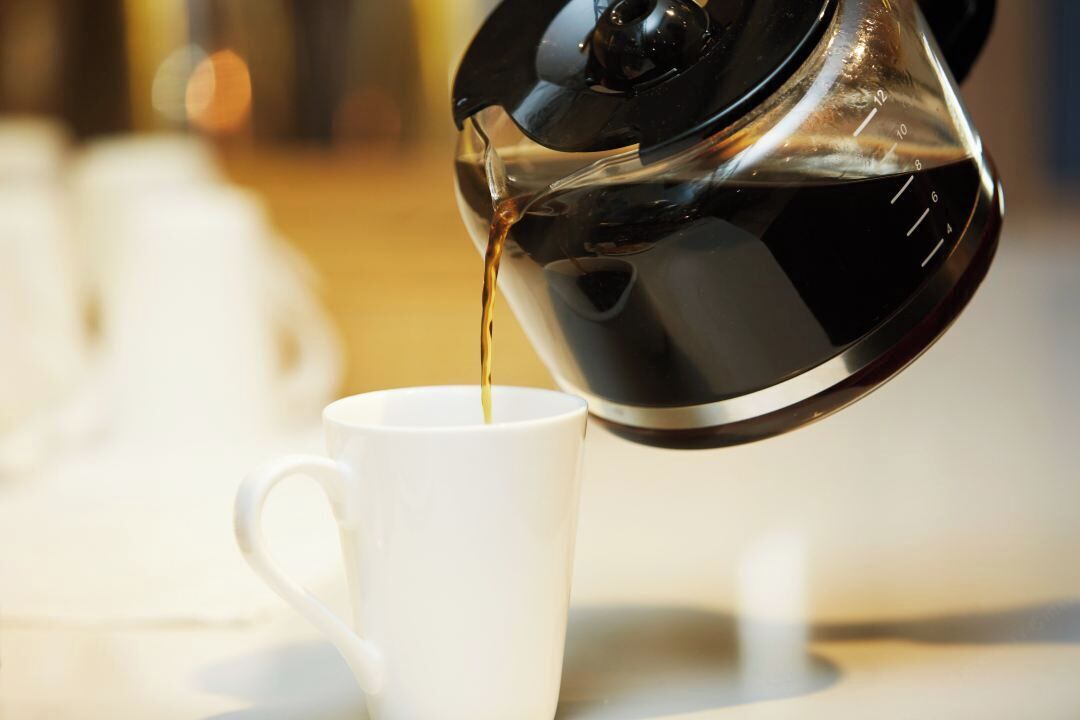 A coffee pot pouring liquid into a white cup.