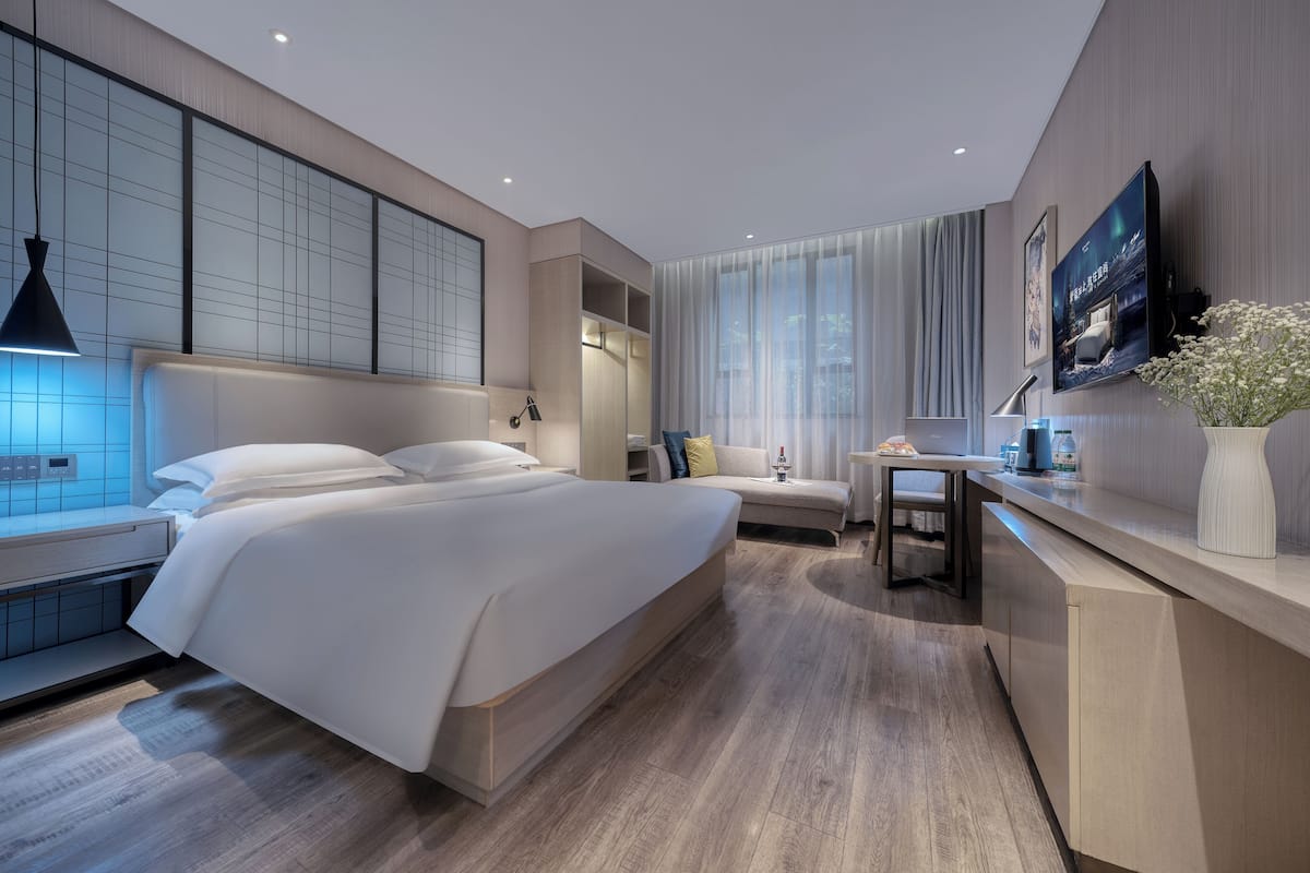 Une chambre d’hôtel moderne, dotée d’un grand lit, d’un bureau, d’une télévision et d’une fenêtre avec des rideaux.