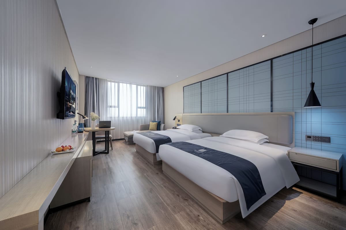 Une chambre d’hôtel moderne équipée de deux lits, d’un bureau, d’une télévision à écran plat et d’une grande fenêtre.