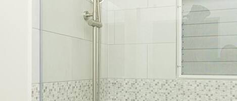 A glass-enclosed shower with a handheld showerhead and a wall-mounted control panel.