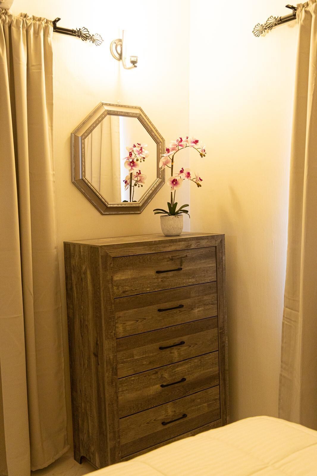 A wooden dresser with drawers, a mirror, and a potted orchid.