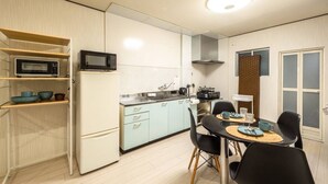 A compact kitchen with a microwave, stove, and sink, a dining area with a table and chairs, and a window with blinds.