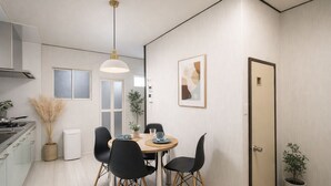 A modern kitchen with a dining area, featuring a round table, black chairs, a hanging light fixture, and a door with a plant beside it.