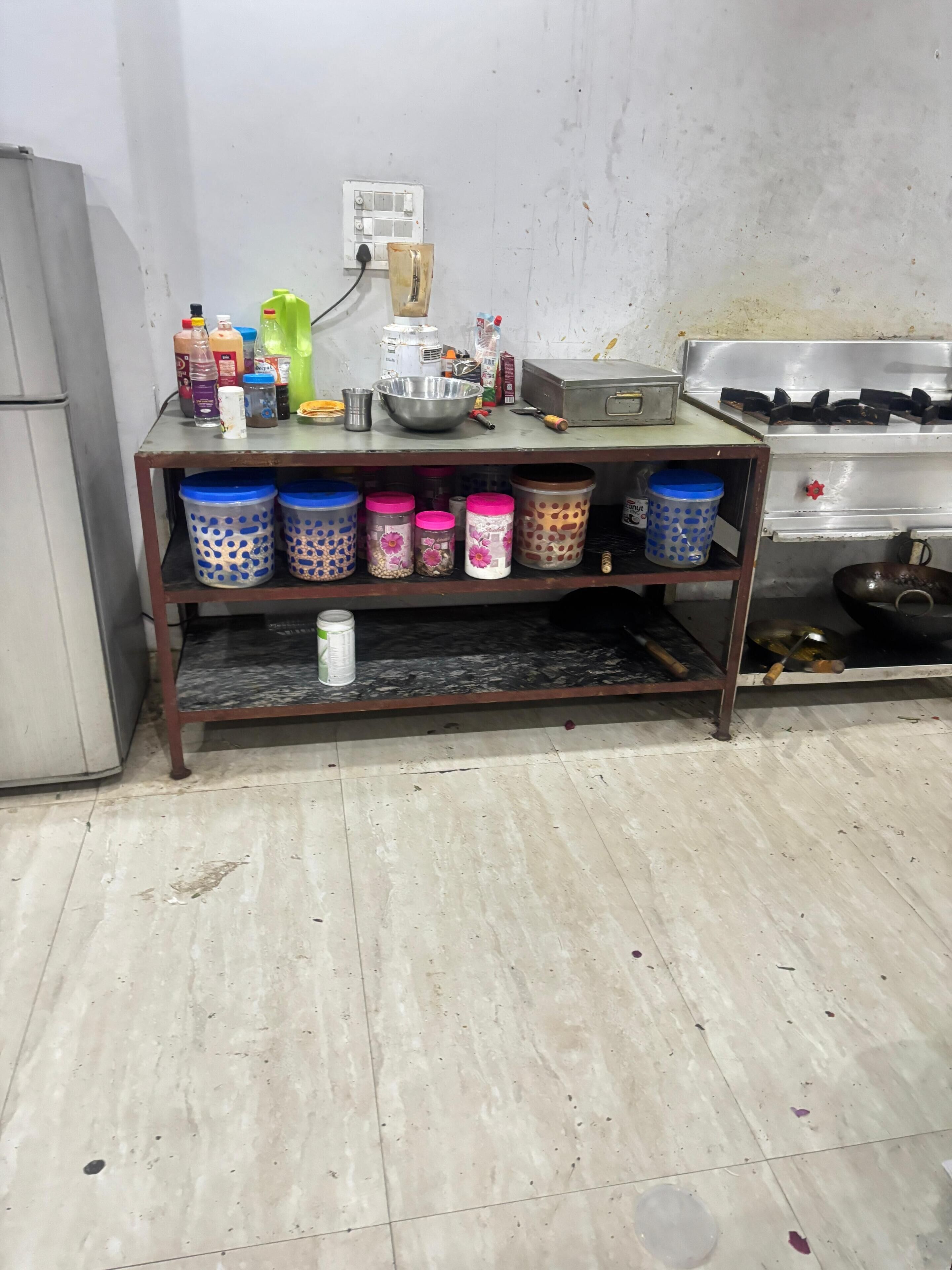 A kitchen with a shelf holding various containers, a gas stove, and a refrigerator.