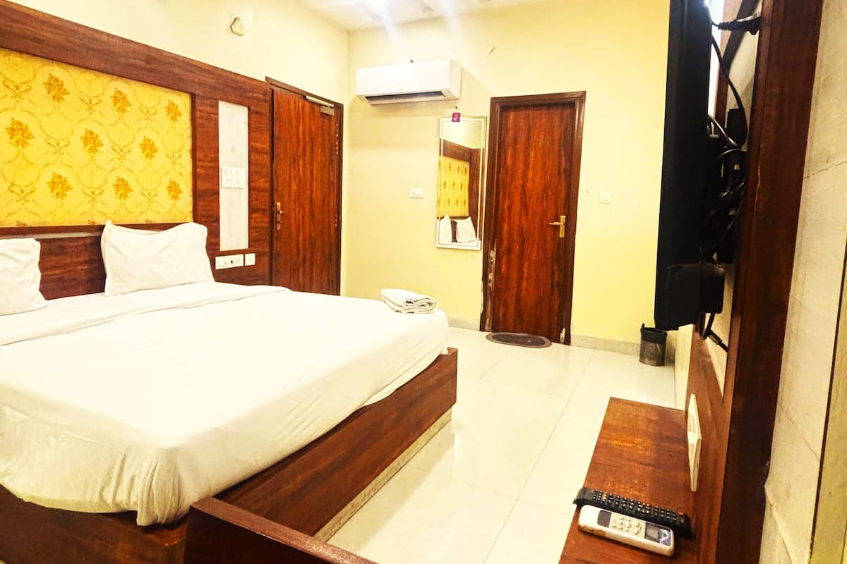 A hotel room with a bed, a desk, a chair, a TV, and an air conditioning unit.