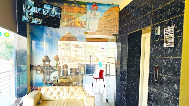 A lobby with a beige sofa, a red chair, a digital elevator display, and a mural of a historical building. - Hotel Hari Inn  (Jaipur)
