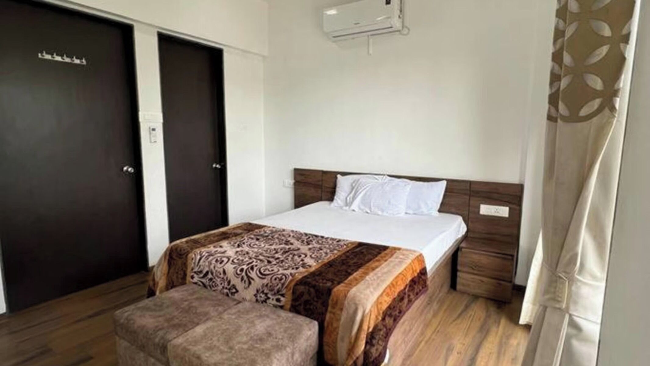 Una habitación de hotel con cama, banca, armario y aire acondicionado de pared.