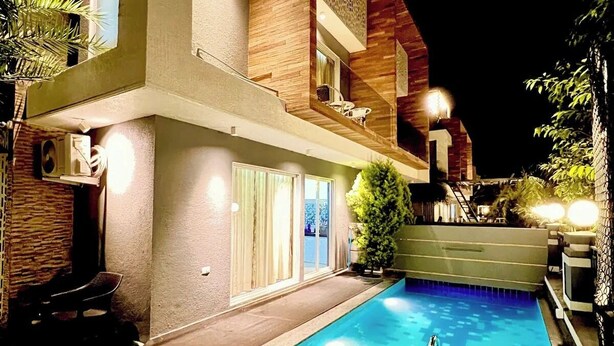 Un moderno edificio de dos pisos con piscina, mobiliario exterior y un patio bien iluminado.