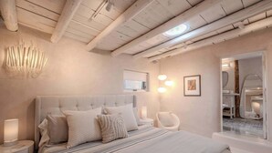 A modern bedroom with a large bed, bedside lamps, a round mirror, and a view of a bathroom.