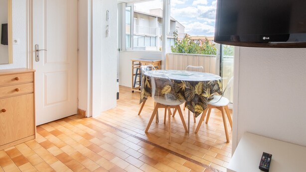 A room with a wooden floor, a dining table with chairs, a TV mounted on the wall, and a door leading to another room. - Bright apartment for 5 ppl, Bright flat for 5 people, close to the sea (Agde)