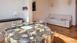 A room with a round table, a sofa, a lamp, and a wall-mounted TV. - Bright apartment for 5 ppl, Bright flat for 5 people, close to the sea (Agde)