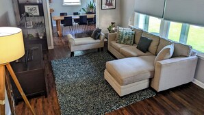 A living room with a sofa, ottoman, and a dining area in the background.