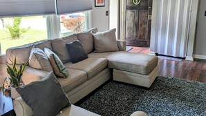 A living room with a sectional sofa, a small table with a plant, and a door with a circular glass window.