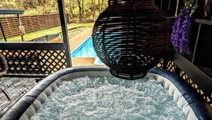 A hot tub with a wooden deck and a view of a swimming pool.