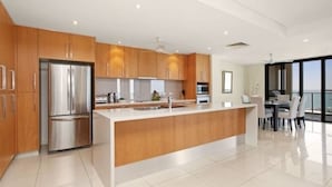 A modern kitchen with wooden cabinets, a stainless steel refrigerator, and a large island with a sink. - Zenlux 4BR Waterfront Penthouse Pad 270 Panoroma (Darwin)