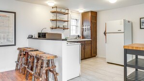 A compact kitchen with a white refrigerator, wooden cabinets, a built-in shelf unit, and a bar stool area. - Hike, Ski & More: Walkable Downtown Granby Home (Granby)