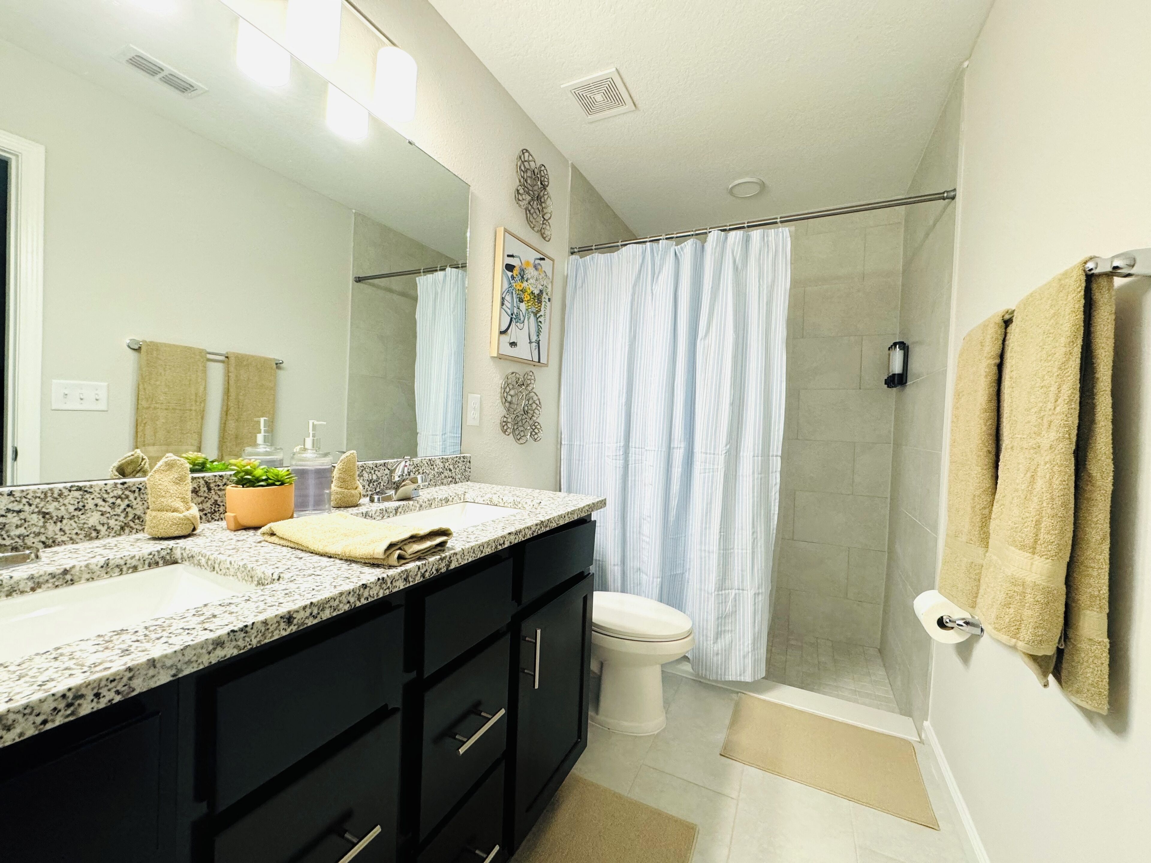 A modern bathroom with a granite countertop, black cabinets, a white toilet, and a glass shower enclosure.