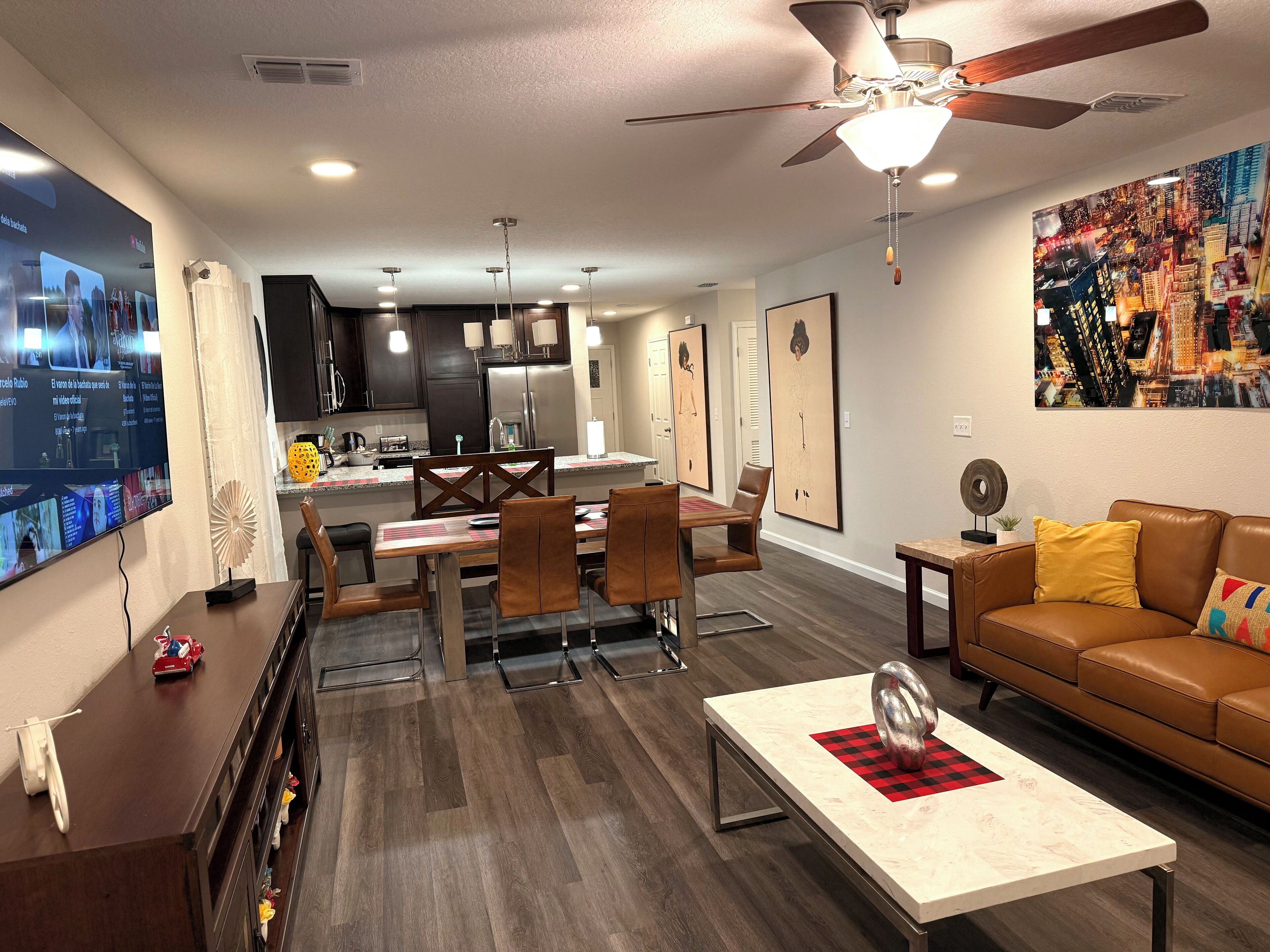 A modern living room with a dining area, a kitchen in the background, and a ceiling fan.