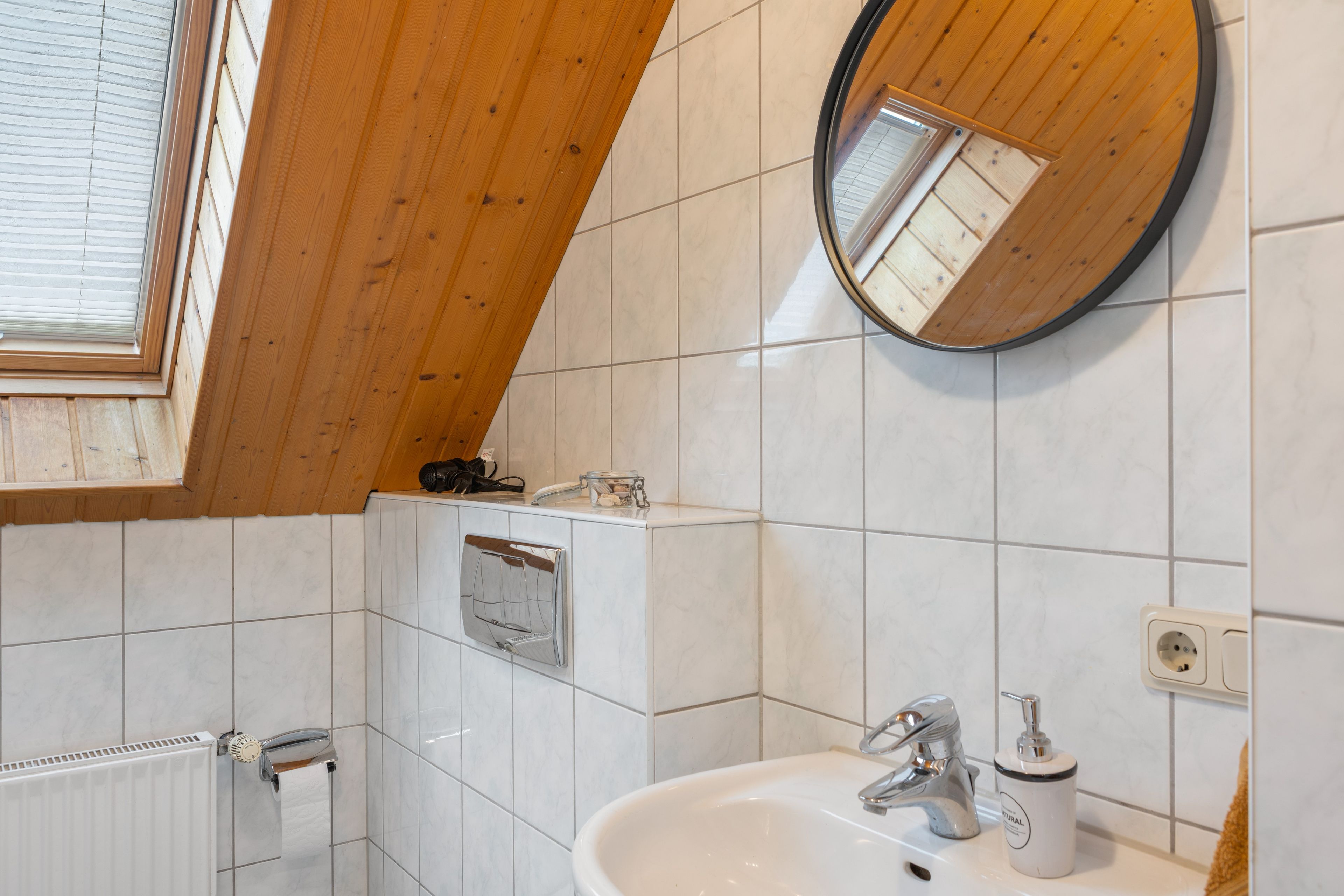 Une salle de bain avec un lavabo blanc, un miroir et une fenêtre avec des stores.