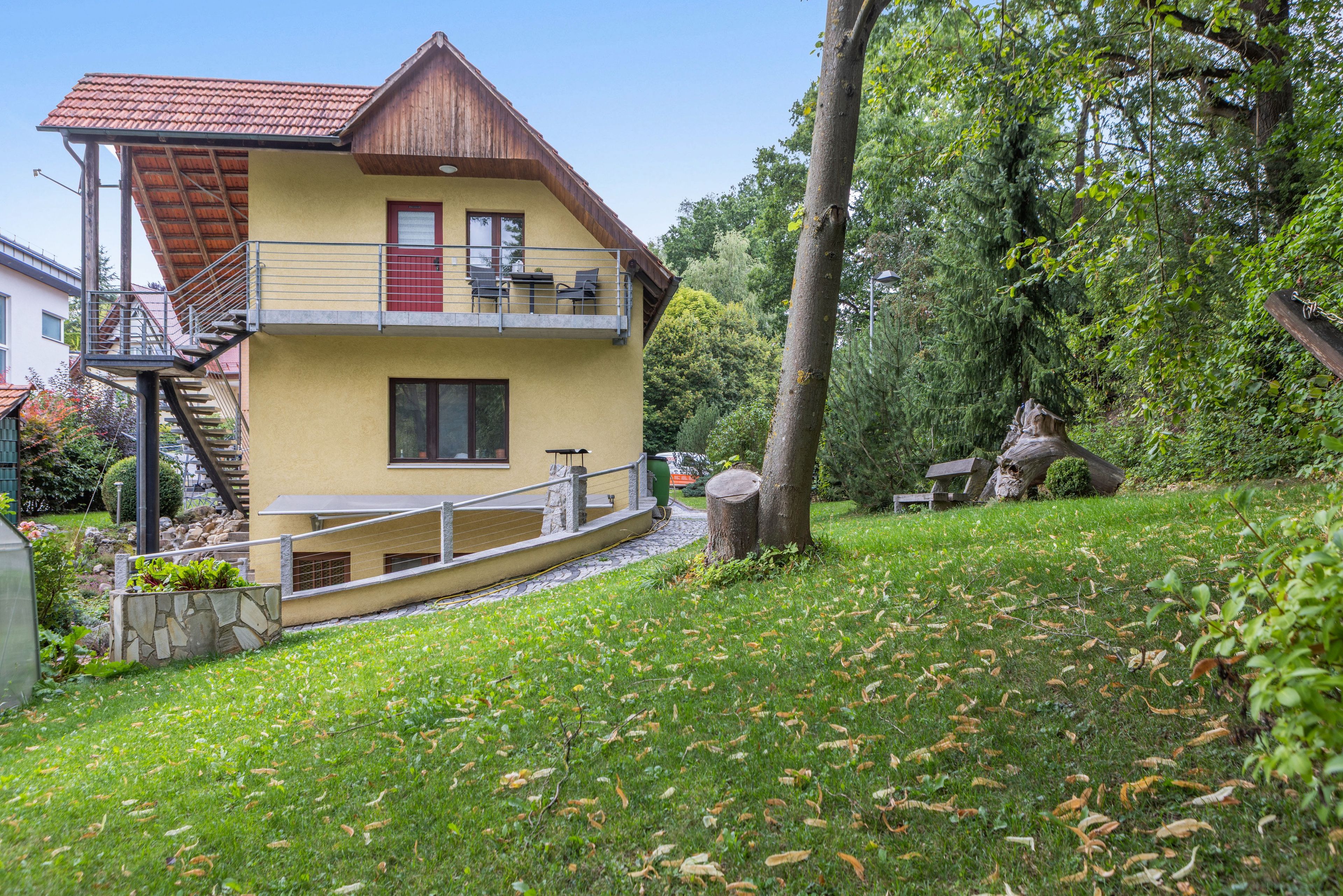 Ein zweigeschossiges Haus mit einem Balkon, umgeben von einem Garten und Bäumen.