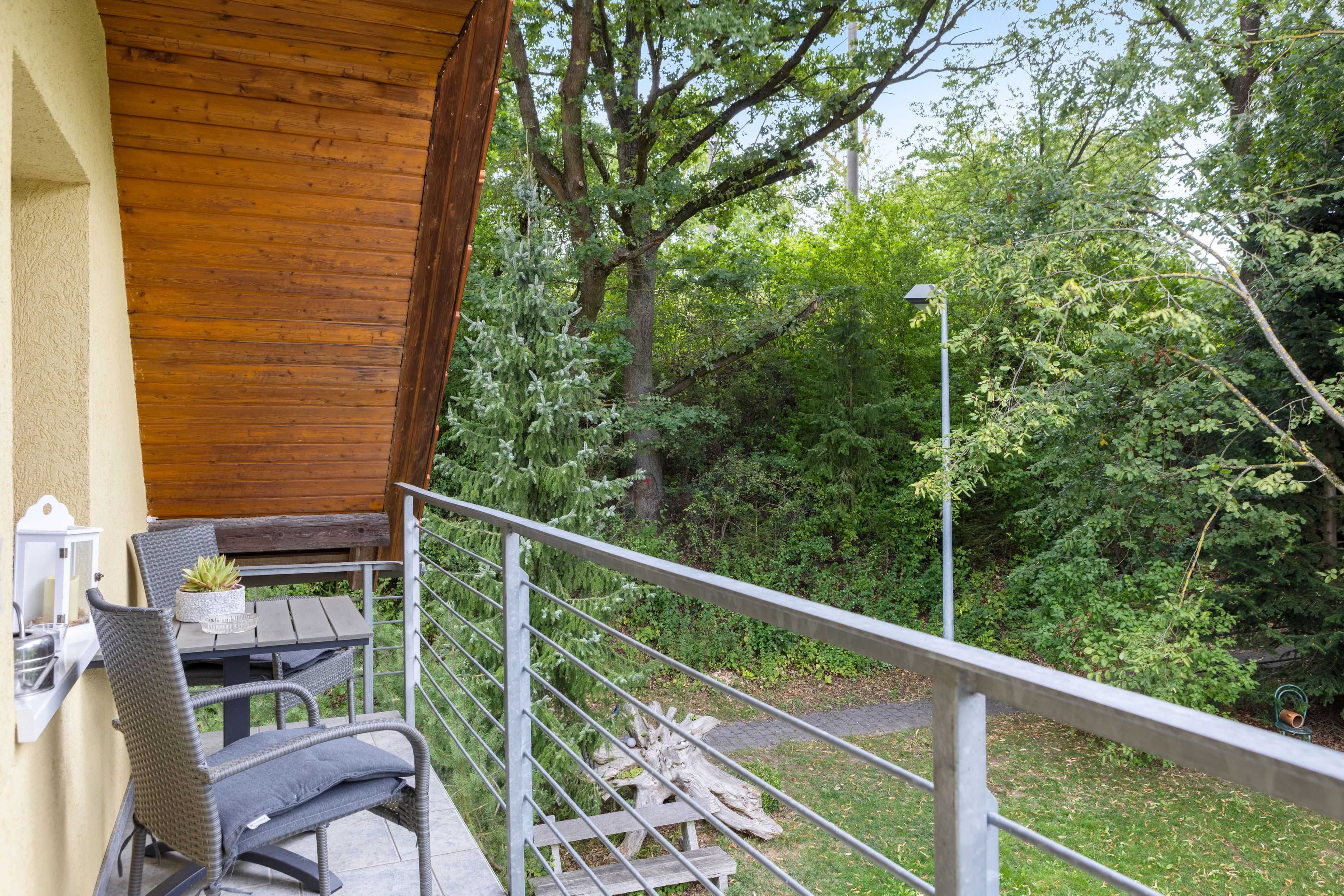 Ein Balkon mit Korbmöbeln, einem Holztisch und einem Blumentopf.