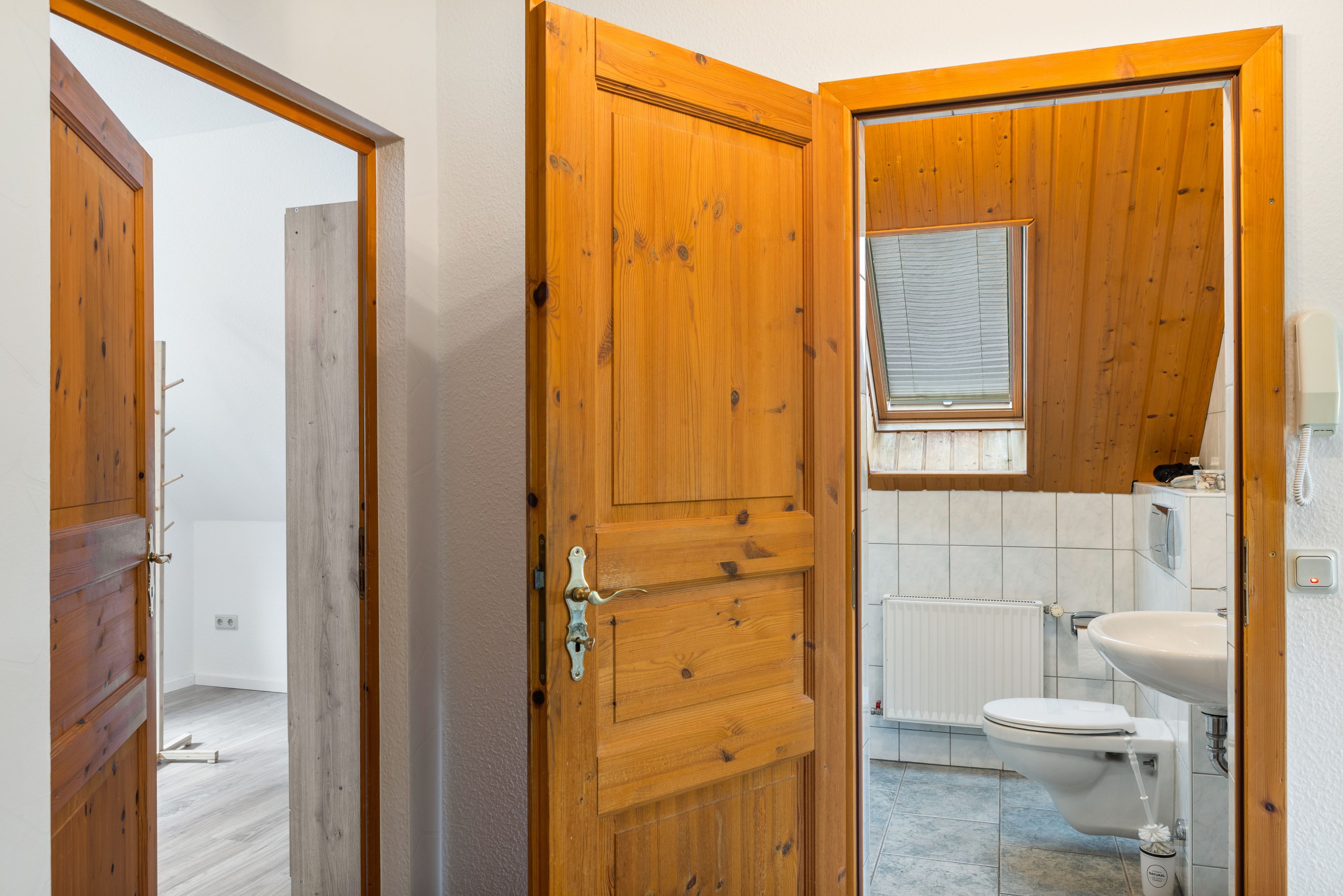 Eine Holztür, die zu einem Badezimmer mit Toilette, Waschbecken und Fenster führt.