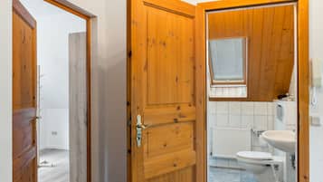 Eine Holztür, die zu einem Badezimmer mit Toilette, Waschbecken und Fenster führt.