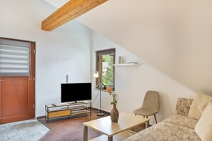 A modern living room with a flat-screen TV, a coffee table, a sofa, a chair, and a window with a view of greenery. - Apartment 'Gaßmann' with Shared Garden, Balcony and Wi-Fi (Wingerode)