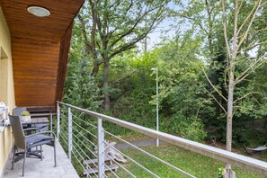 Un balcon agrémenté d’une table et de chaises, entouré d’un mur en bois et d’une rambarde en métal, donnant sur un jardin luxuriant.