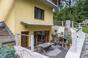Un bâtiment à deux étages, à la façade jaune, doté d’un balcon avec une rambarde en métal et d’un escalier en pierre menant à l’entrée.