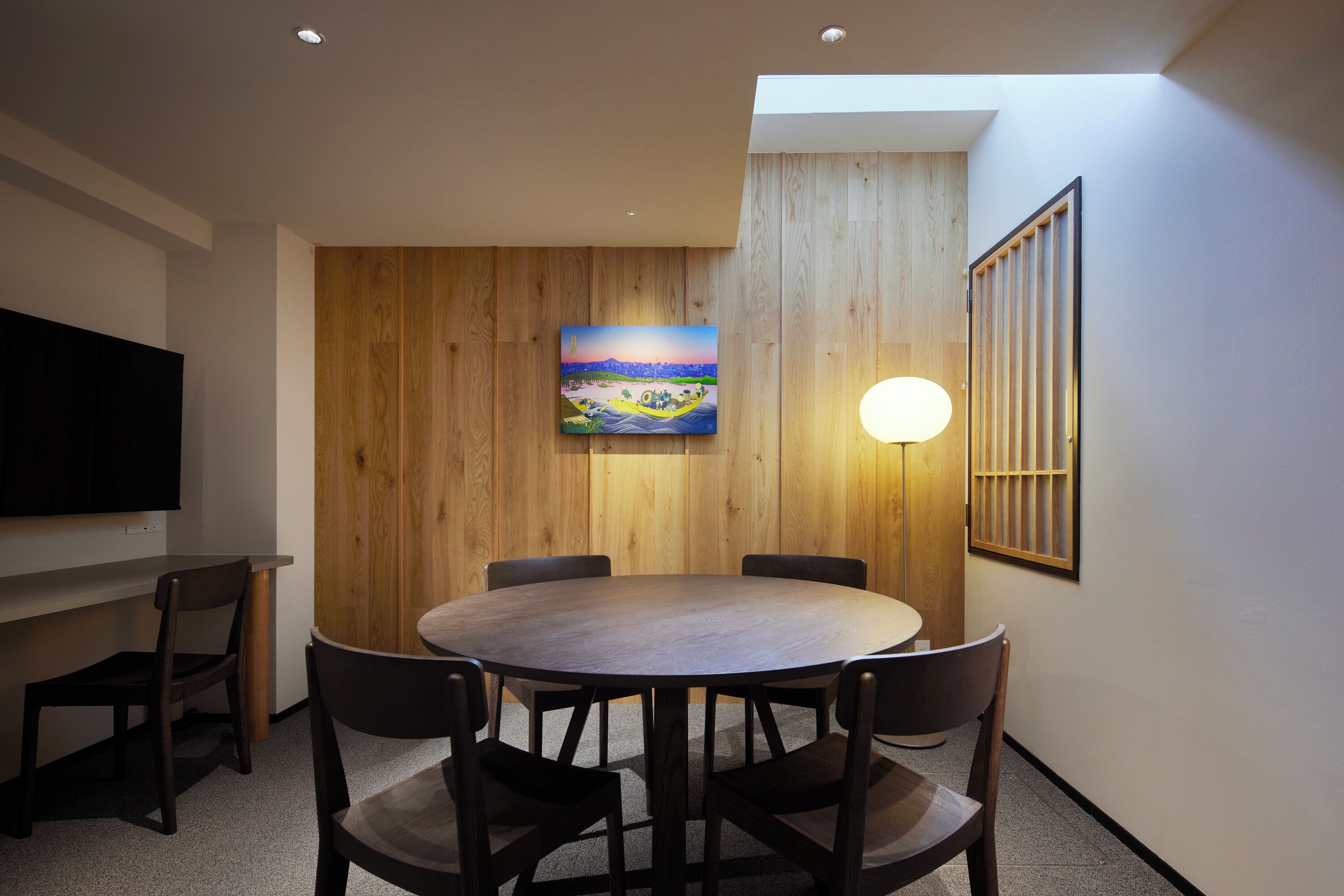 Uma sala de jantar moderna com uma mesa redonda, seis cadeiras, um quadro na parede e uma TV fixada na parede.