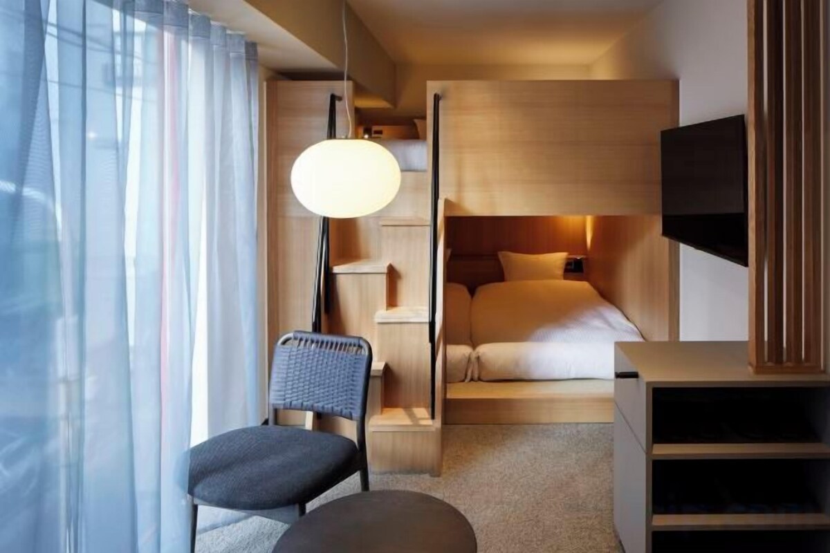 A compact hotel room with a bed, a desk, a chair, a TV, and a large window with curtains.