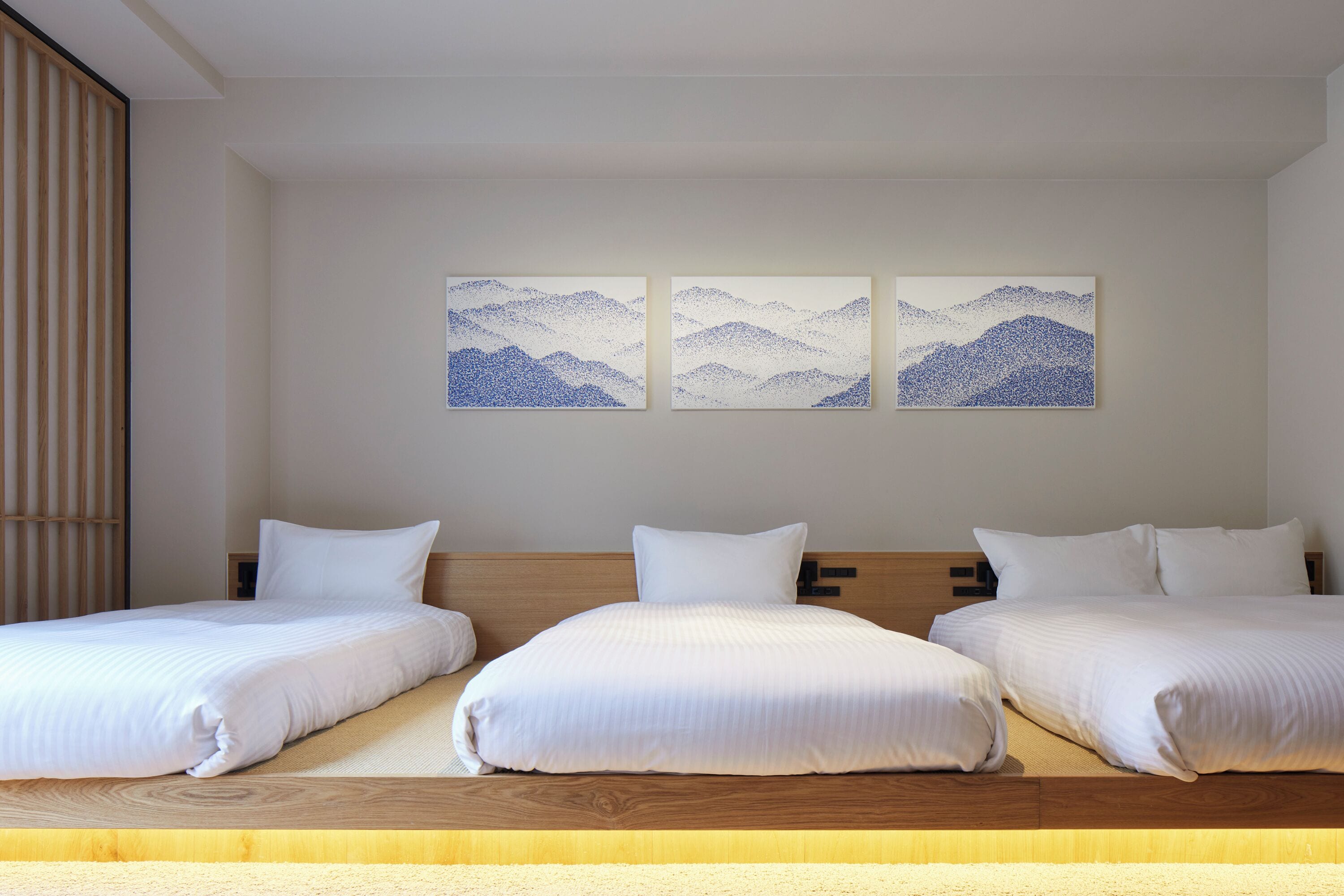Een hotelkamer met drie bedden, houten hoofdeinden en drie schilderijen van berglandschappen aan de muur.