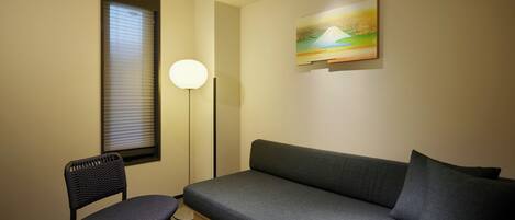 Een kamer met een bank, een stoel, een vloerlamp en een schilderij aan de muur.