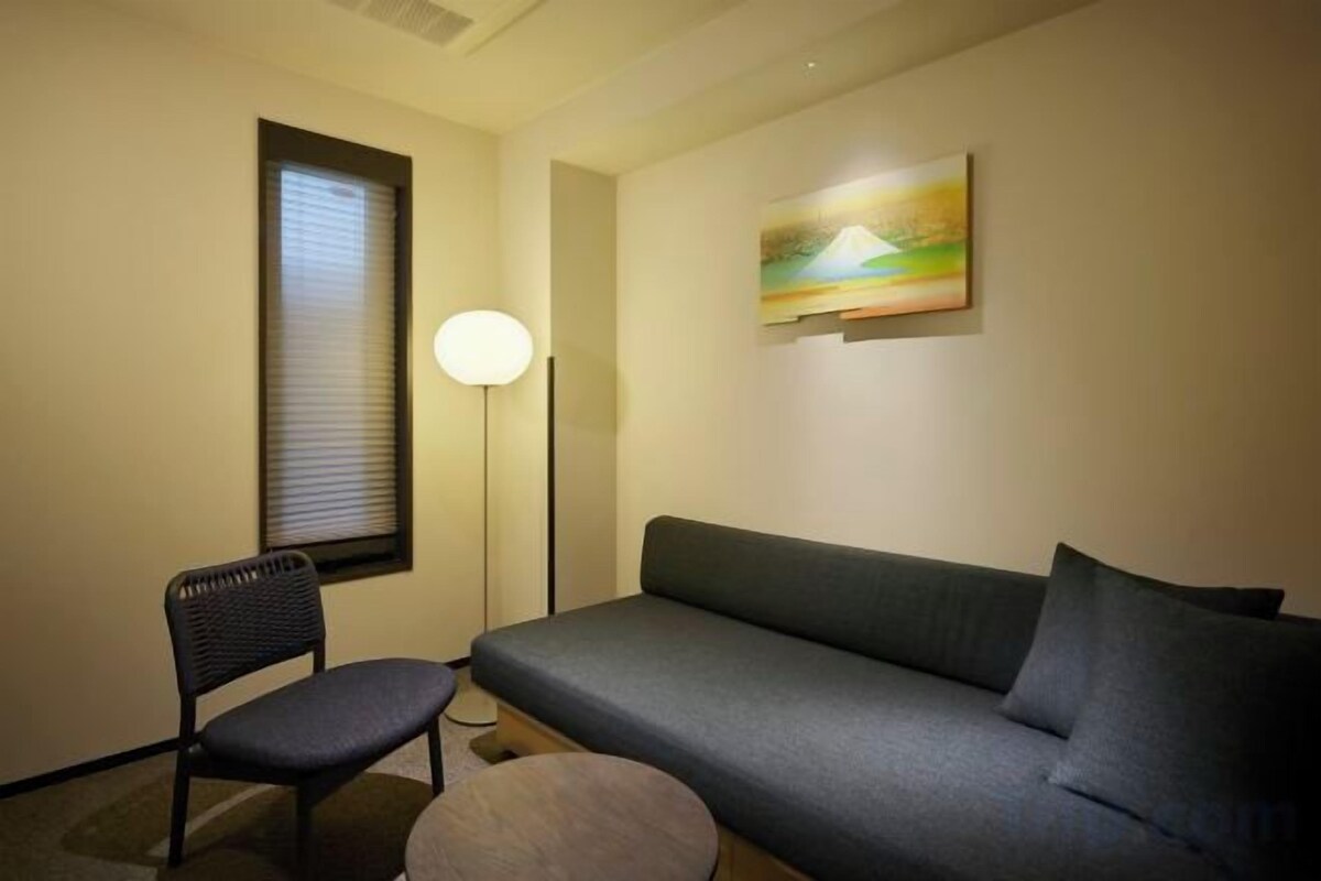 A room with a sofa, a chair, a floor lamp, and a painting on the wall.