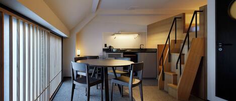 A modern kitchen with a dining area, wooden staircase, and a view of the outside.