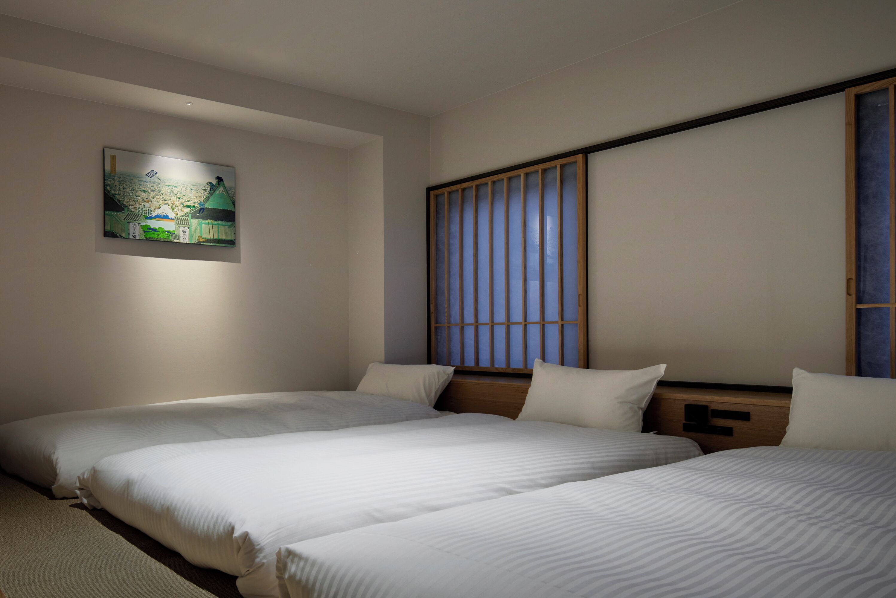 A hotel room with two beds, a painting on the wall, and a sliding door with a view.