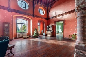 A spacious room with wooden floors, large arched windows, a fireplace, and a Christmas tree.