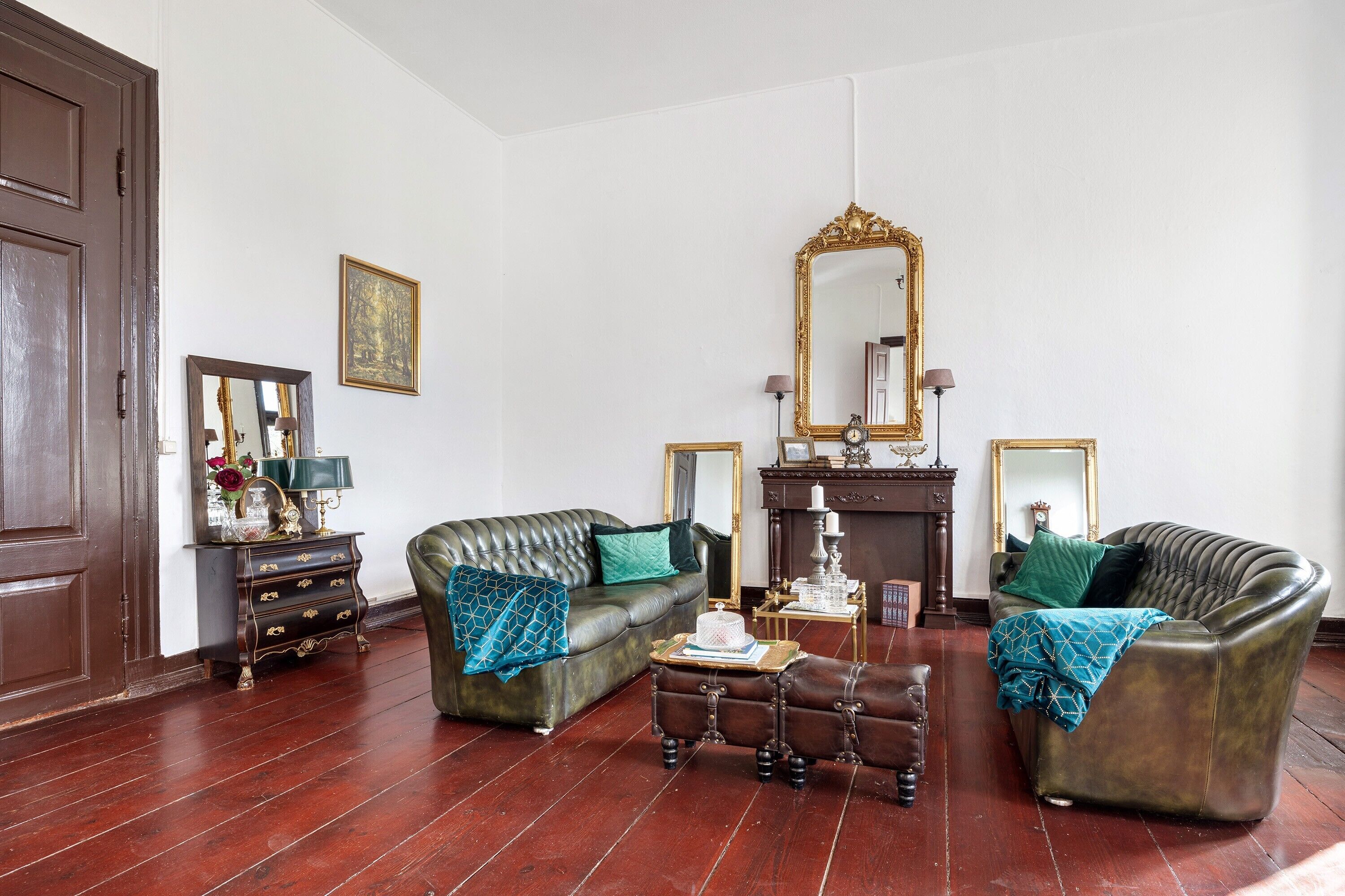 Een kamer met een bank, fauteuil en een kleine tafel met een lamp.