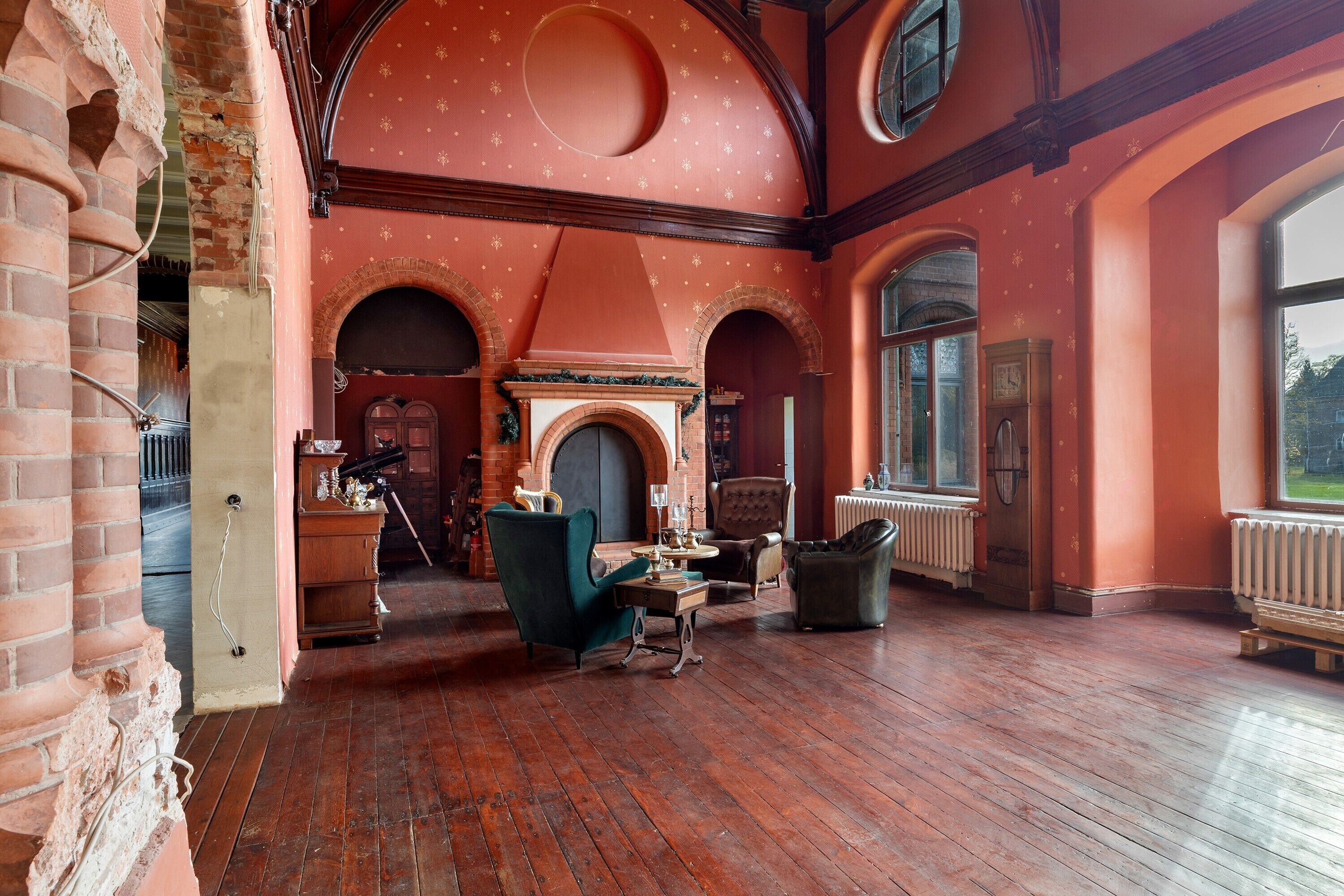 A spacious room with a fireplace, wooden flooring, and arched windows.