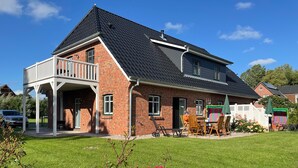 A two-story house with a balcony, a patio with outdoor furniture, and a well-maintained lawn.