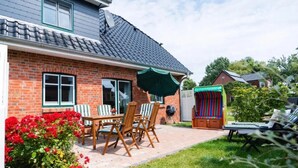 Une maison avec une façade en briques, un toit en tuiles, une terrasse avec une table et des chaises, et une tente de jeu aux couleurs vives.