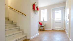 Un escalier avec une rampe, une bouée de sauvetage accrochée au mur, une fenêtre avec vue et une porte.
