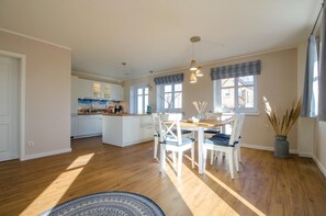 A spacious kitchen with a dining area, wooden flooring, and large windows.