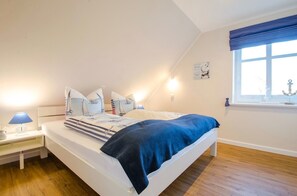 A bedroom with a bed, bedside tables, a window with curtains, and a wall decoration.