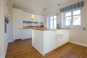 A modern kitchen with white cabinetry, a wooden island, and a large window with a view.