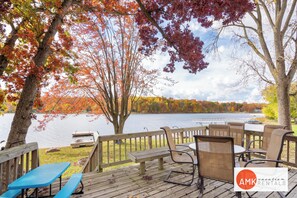 A wooden deck with outdoor seating, overlooking a lake with autumn foliage.