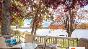 Une terrasse avec une table et des chaises donnant sur un lac, entourée d’arbres aux feuilles d’automne.