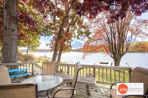 A deck with a table and chairs overlooking a lake, surrounded by trees with autumn foliage.